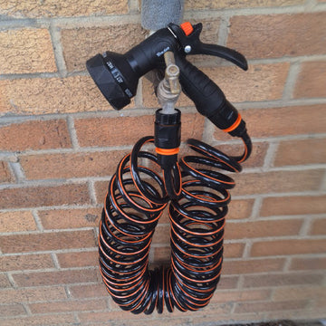Black and orange spiral hose and adjustable spray gun for an outdoor cold-water dog rinse kit.